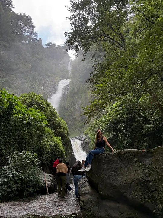 Visitante sentada en una roca junto a la cascada